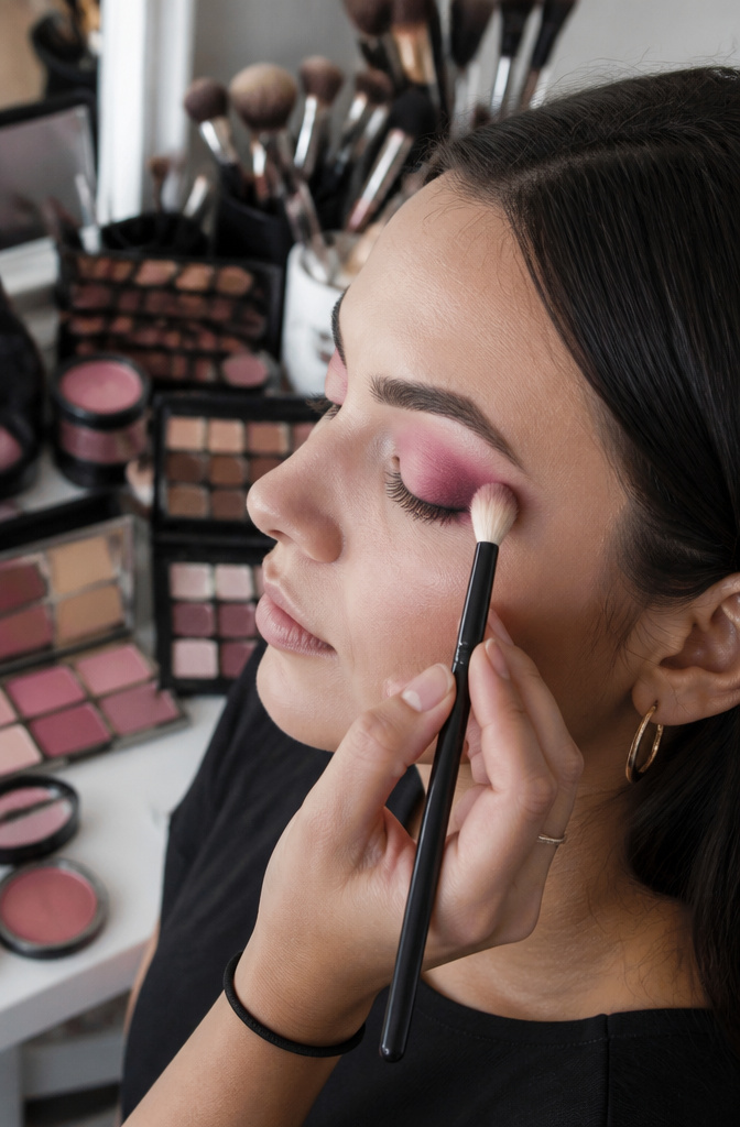 Close-up of a hand blending pink eyeshadow with a fluffy brush.